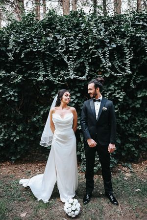 Wedding portrait against lush ivy wall with classic white gown and black tuxedo.