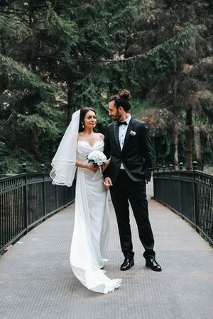 Joyful wedding couple sharing a moment on bridge with evergreen forest backdrop.