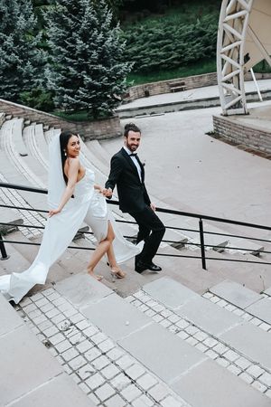 Wedding couple poses playfully on concrete amphitheater steps with evergreen backdrop.