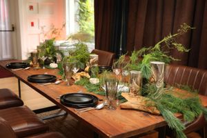 Rustic dining table set with black plates and evergreen centerpiece decorations.