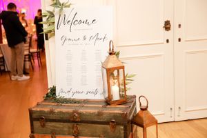 Elegant welcome sign display with vintage trunks and copper lanterns at a wedding reception entrance.