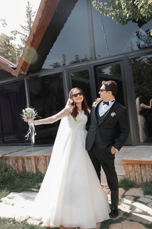 A stylish couple poses outside a modern building in elegant wedding attire.