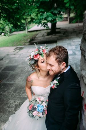 A couple shares a tender moment in a garden setting with the bride wearing a floral crown and holding a bouquet.