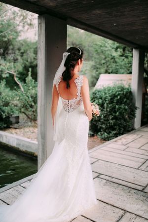 Back view of bride in elegant lace wedding dress with flowing train on covered porch.