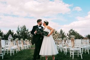A romantic outdoor wedding ceremony setup with white chairs and newlyweds sharing a moment.