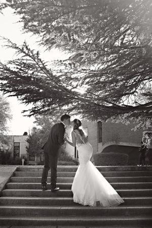 Romantic black and white wedding photo of a couple sharing an intimate moment on stone steps under a tree.