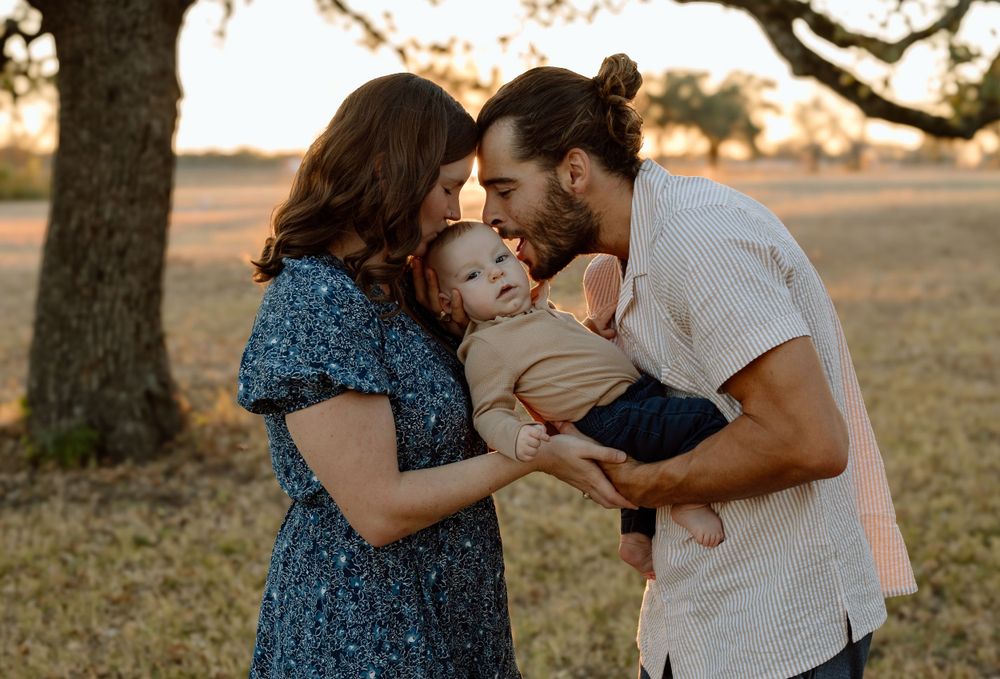 A couple shares an intimate moment with their baby outdoors during sunset.