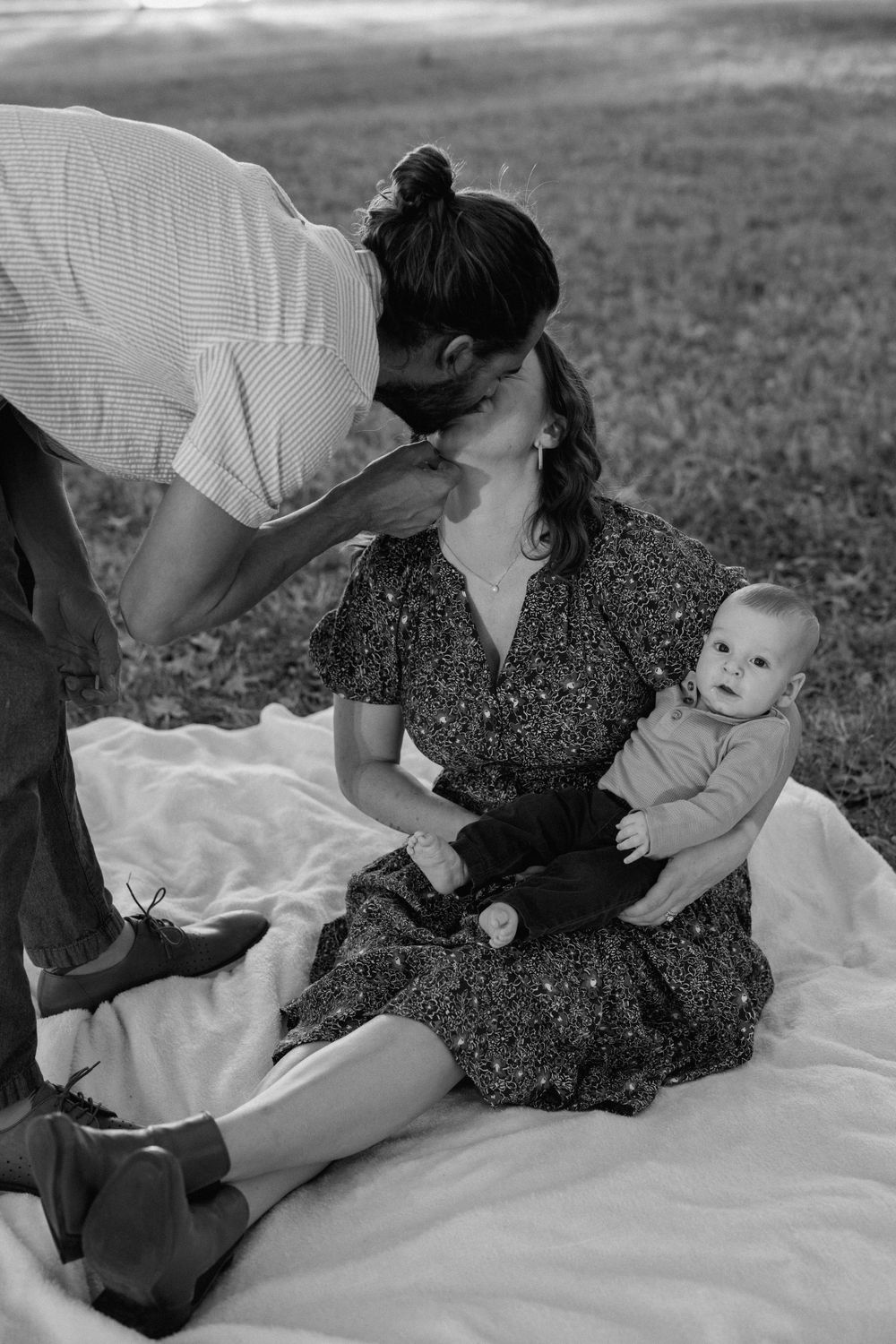 black and white photo of a couple kissing while the mom holds her baby