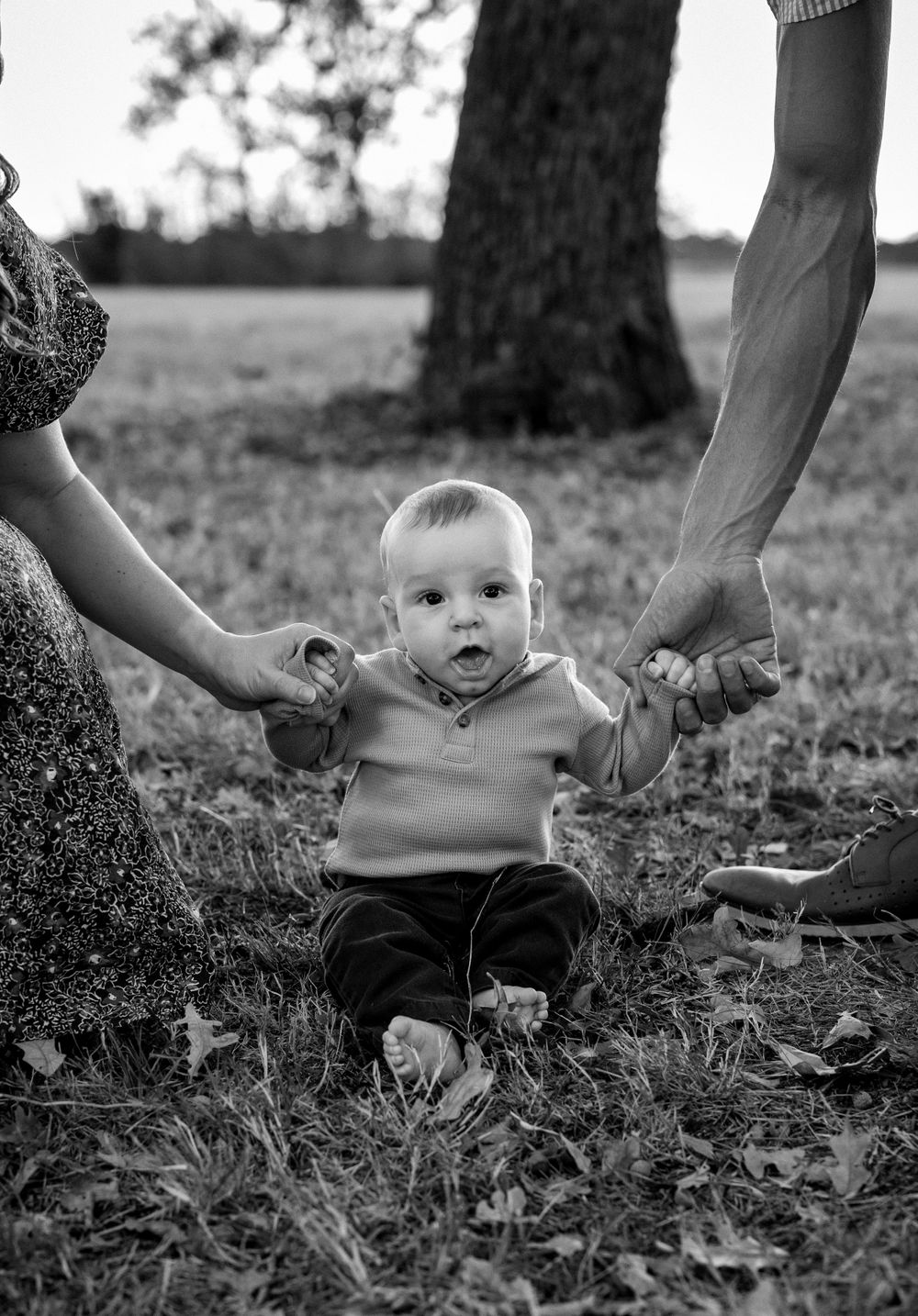 black and white photo of a baby holding parents hands