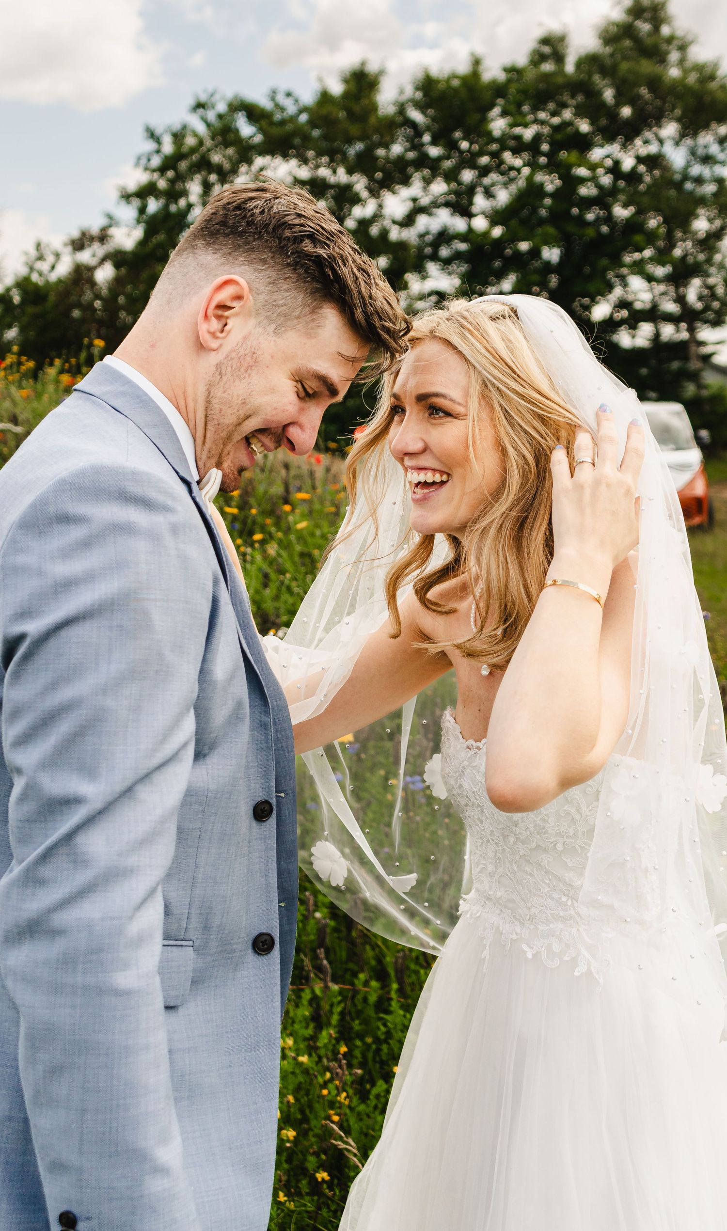 Candid moment of laughter and joy shared between newlyweds in a flower-filled meadow.