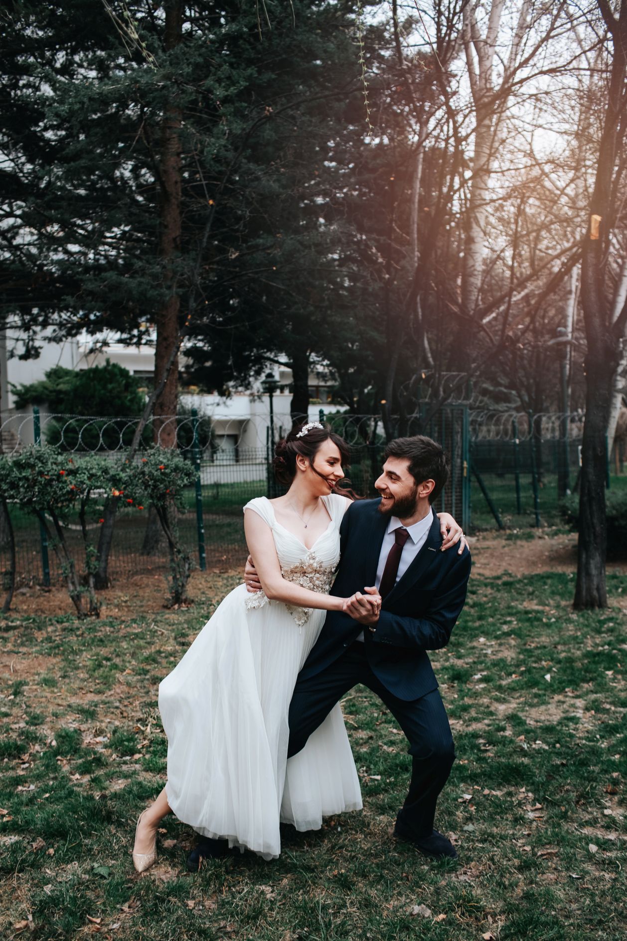 Romantic wedding couple posing playfully in outdoor garden setting at sunset.