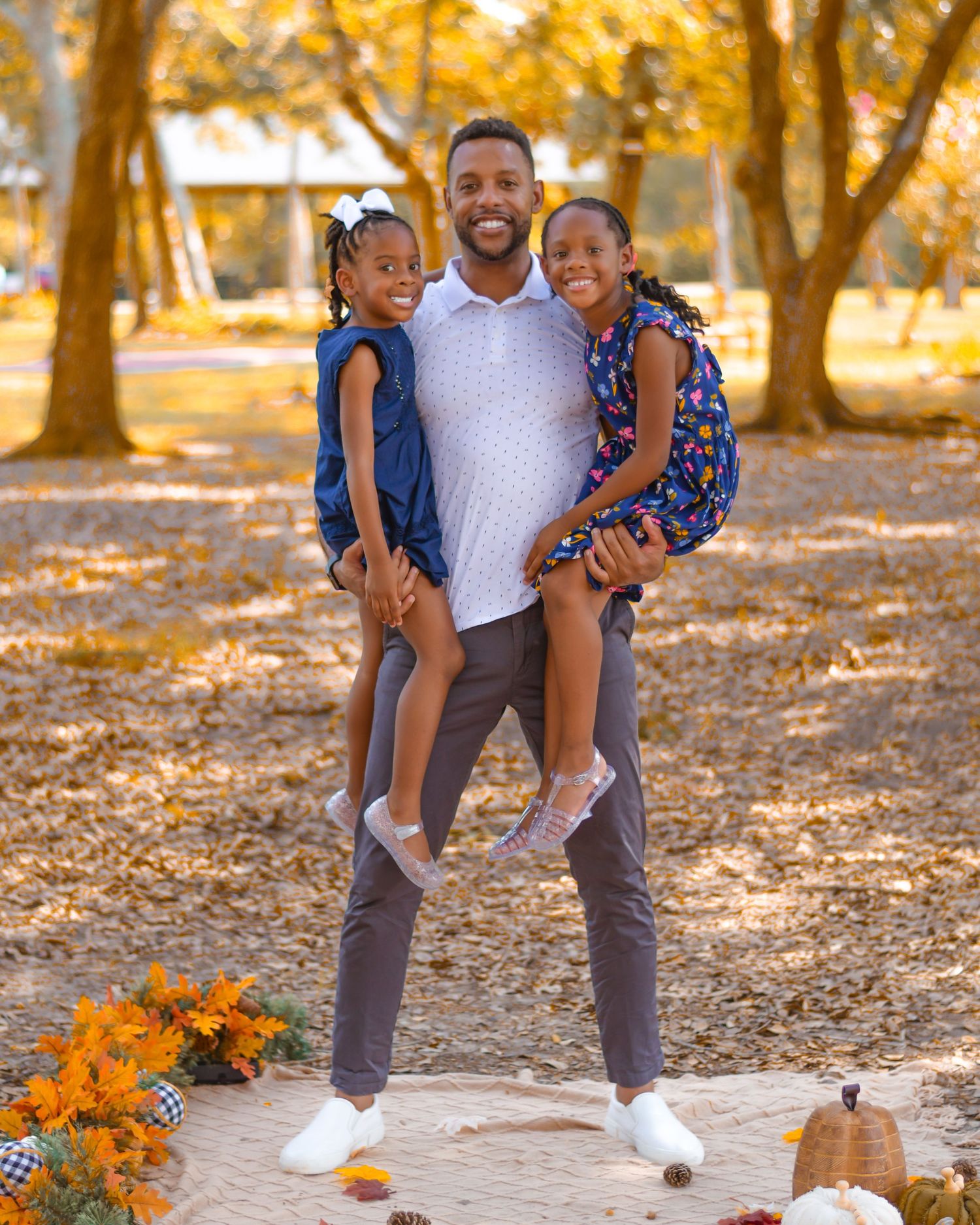 Parent holding two children in matching outfits during autumn photoshoot with pumpkin decorations.