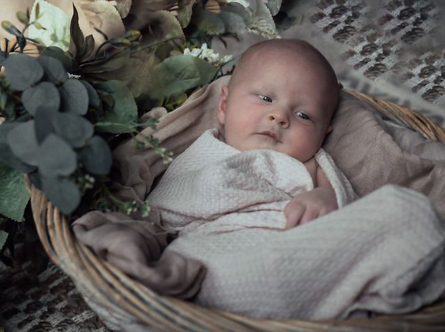 Newborn baby sleeping peacefully in wicker basket with soft neutral toned blankets.