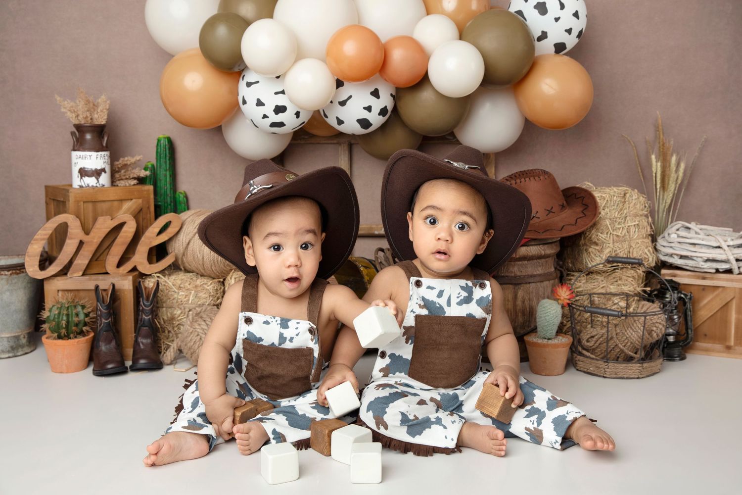 Candid photo of two toddlers in rustic western-themed setup with balloon arch and decorations.