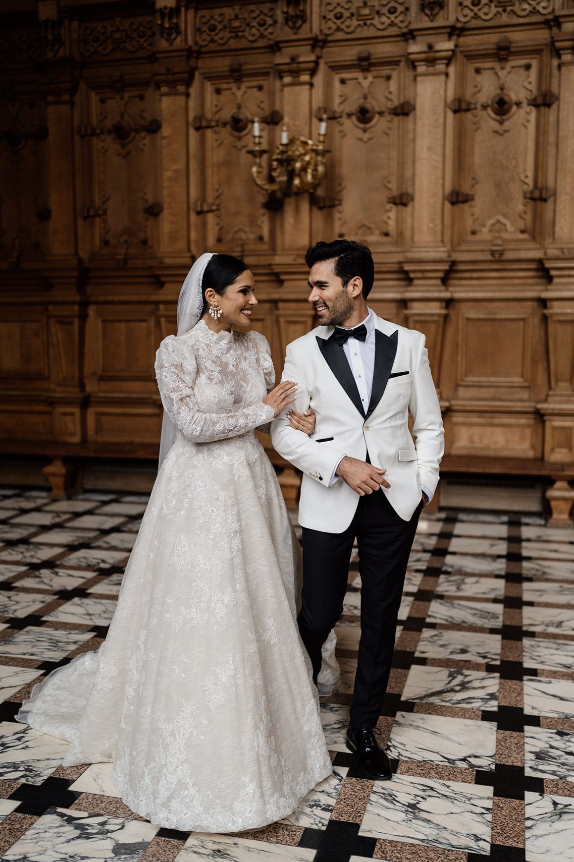 Couple on their wedding day holding onto each other while walking through the grand hall at Harlaxton Manor.