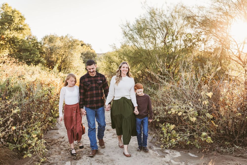Family of four walking hand-in-hand on a sunlit desert path surrounded by lush greenery in beaumont ca