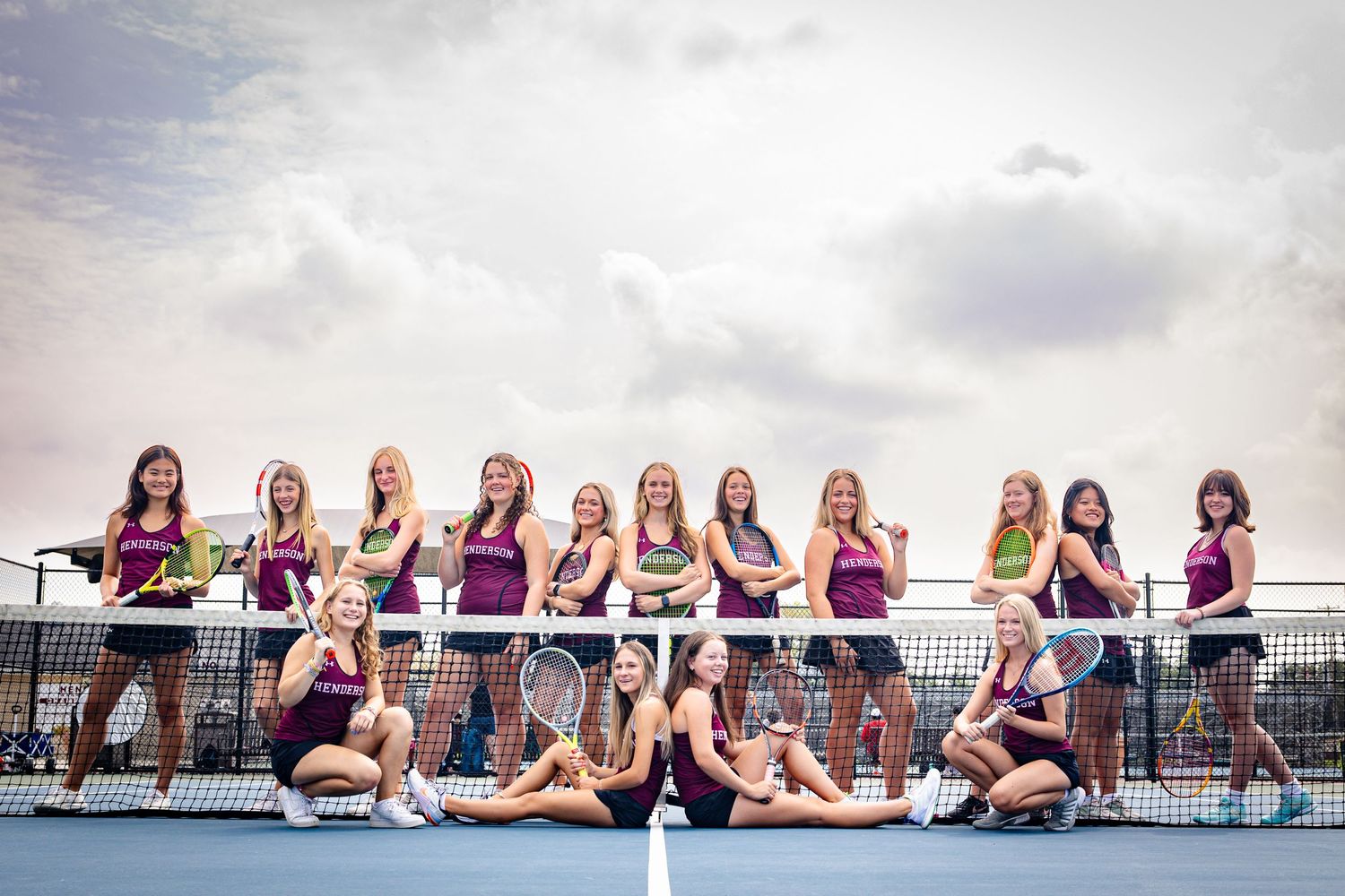 High school tennis team poses for group photo on court with players in purple uniforms.
