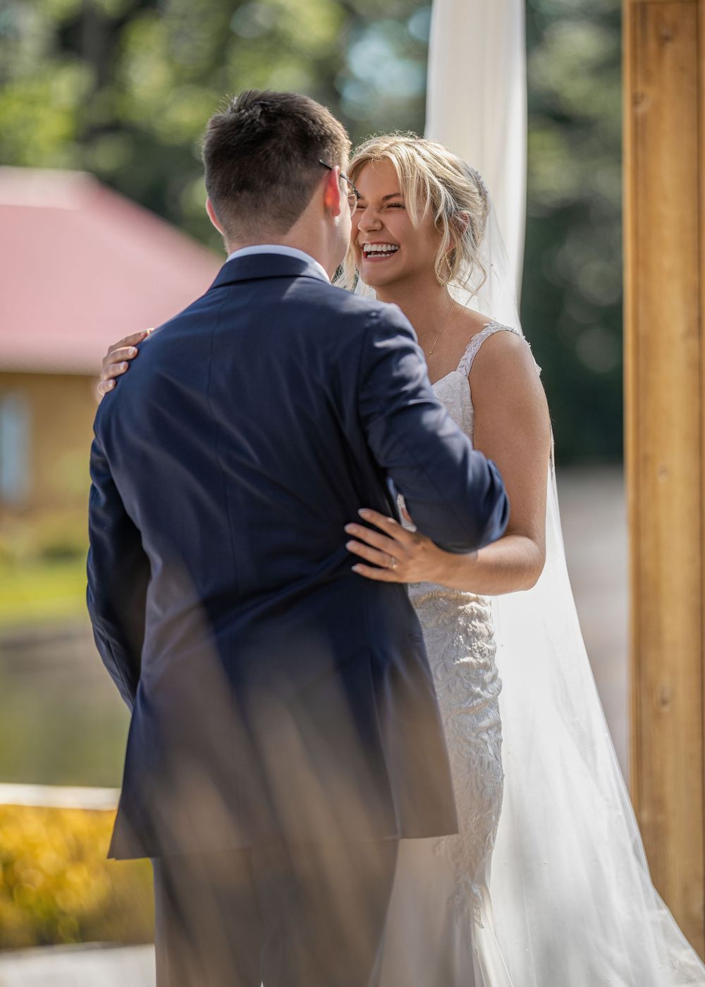 Newly married couple embraces during their wedding ceremony beside a lake on a sunny day.