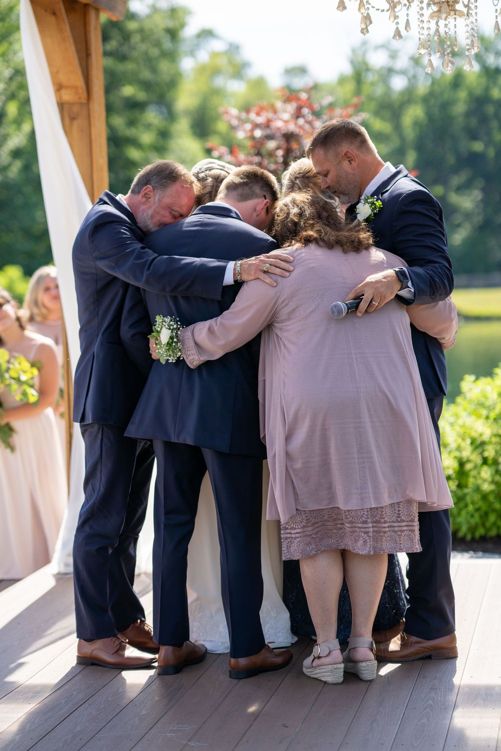 Wedding party shares a playful group hug on a covered porch during outdoor celebration.