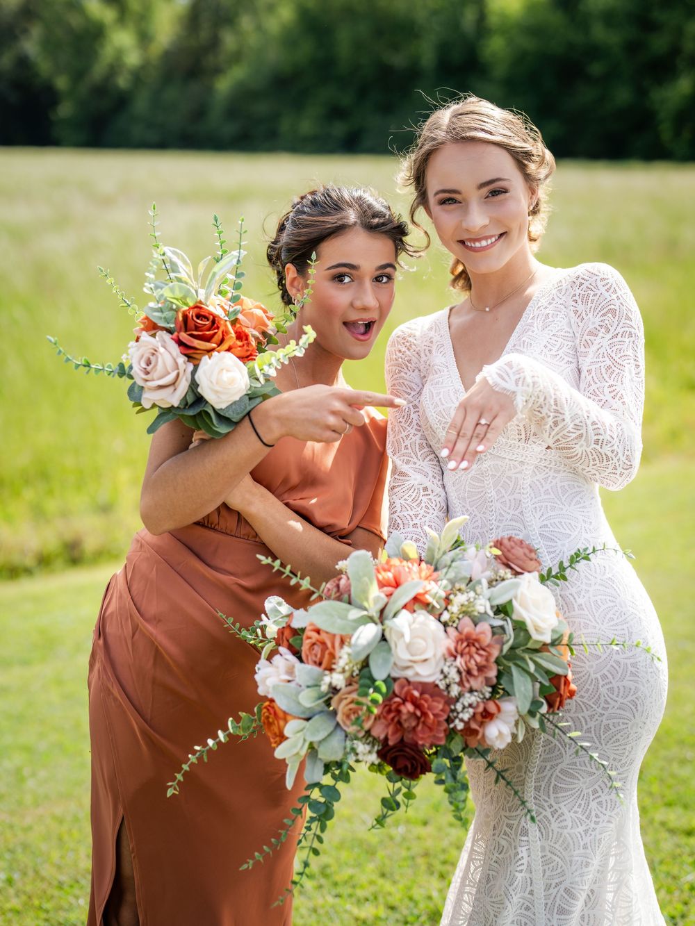 A couple poses outdoors with their wedding attire and colorful coral and white floral bouquets in a sunny field.