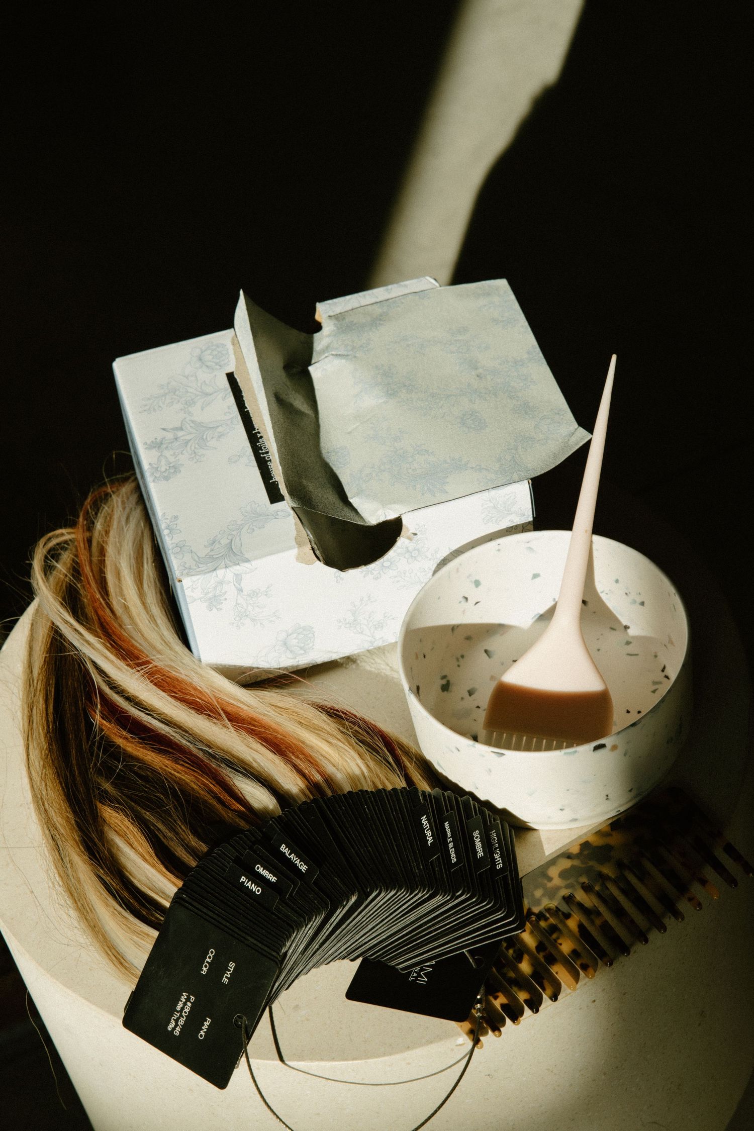 Hair dye supplies including applicator bottles, hair swatches, and mixing bowls arranged on white surface.