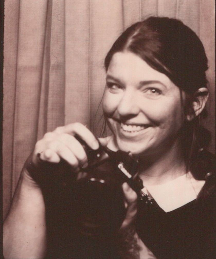 Self portrait of photographer in a vintage photo booth. She is holding up one of the cameras she uses for her business.