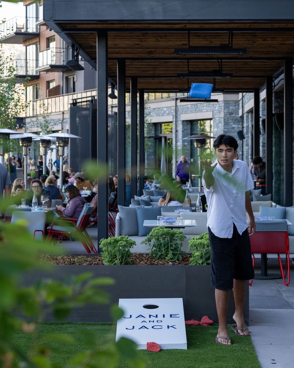 Young man standing on outdoor restaurant patio next to a Janie and Jack shopping bag on a sunny day.