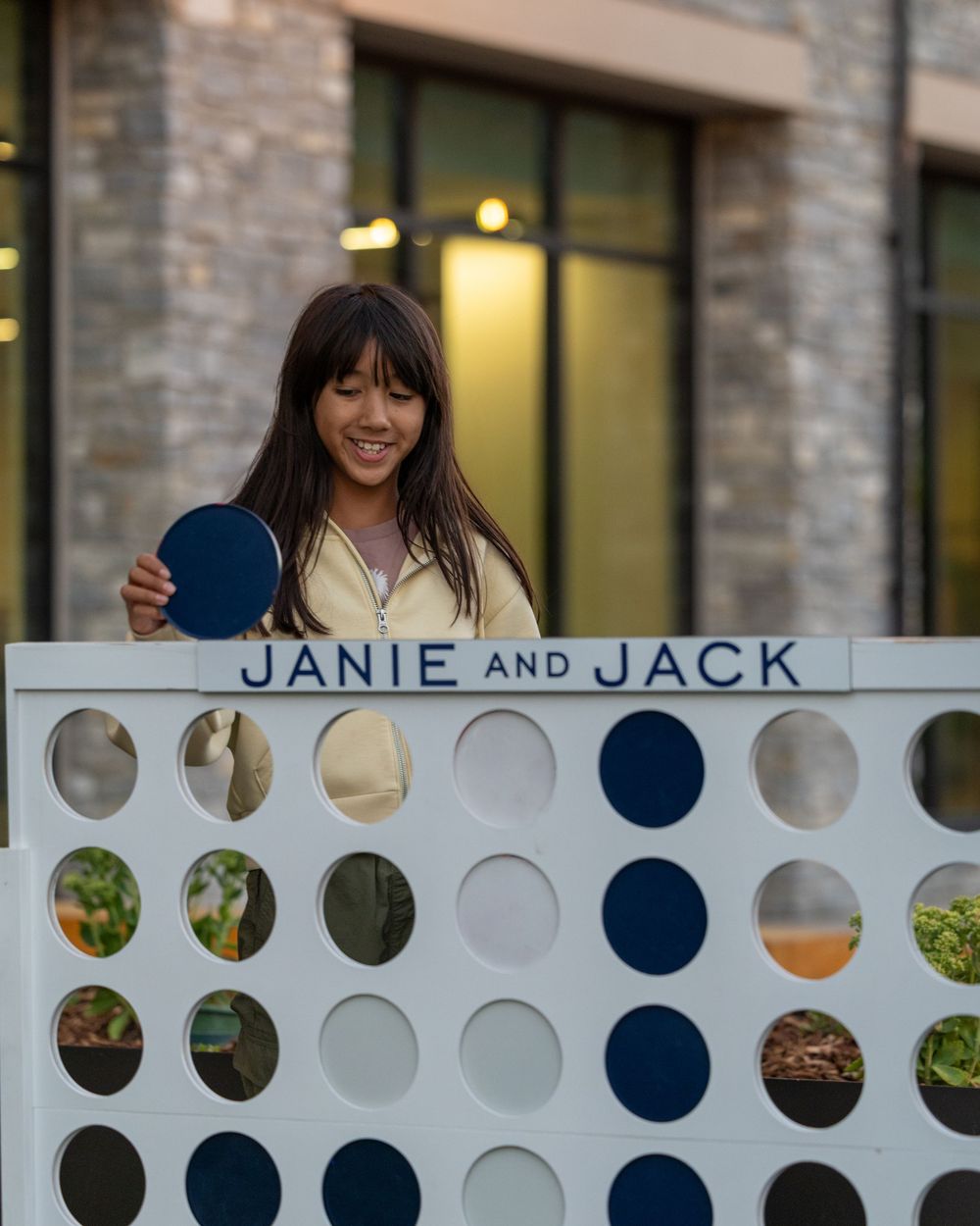 Young woman smiling while playing oversized Connect Four game at a Janie and Jack branded event.