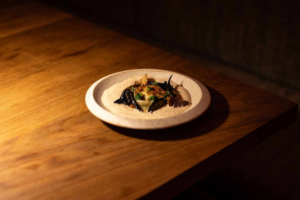Elegant fine dining dish with dark greens and garnish served on a rustic ceramic plate on a wooden table.