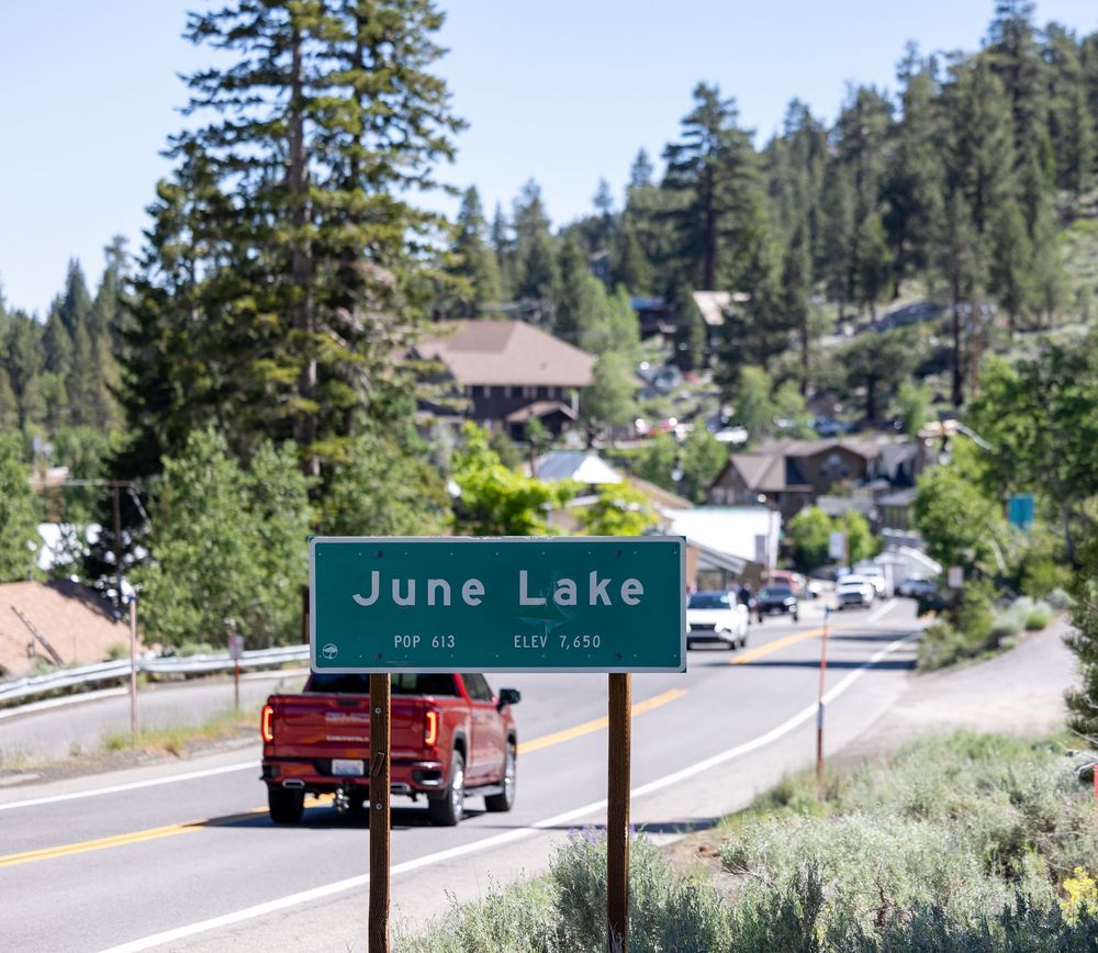 June Lake town entrance sign on a scenic mountain highway in California with pine trees and buildings.