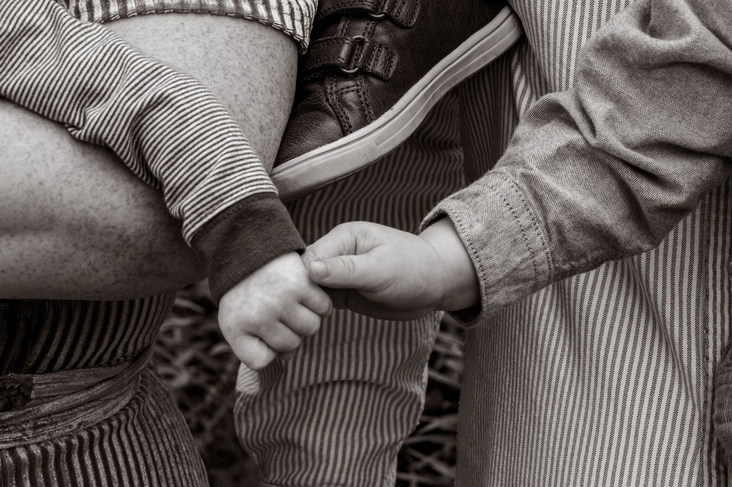Black and white close-up of a baby holding an adult finger in a tender moment.