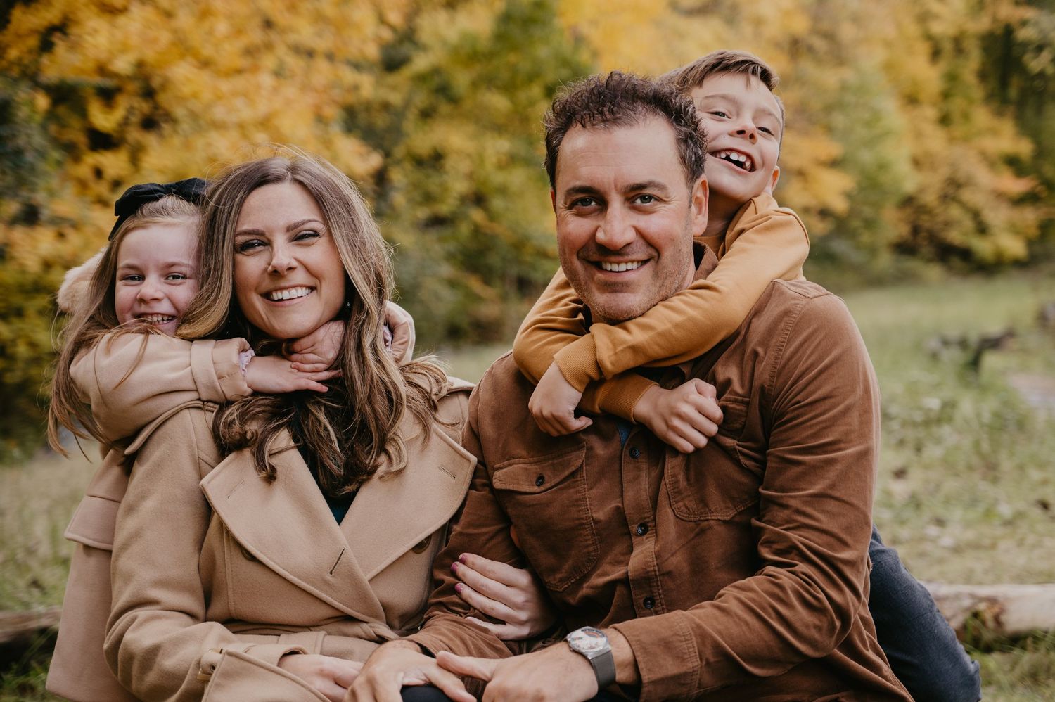 Happy family of four smiling together in a colorful autumn park setting.