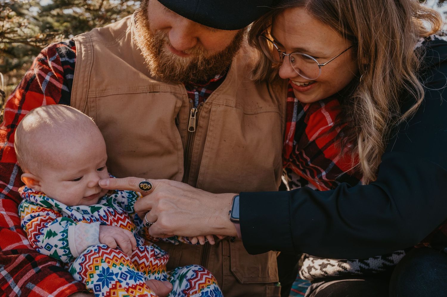 Young couple lovingly gazing at their newborn baby wrapped in a colorful blanket outdoors.