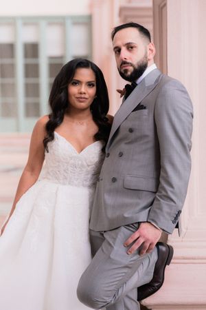 A bride in a white strapless gown and groom in a gray suit pose elegantly together at their wedding.