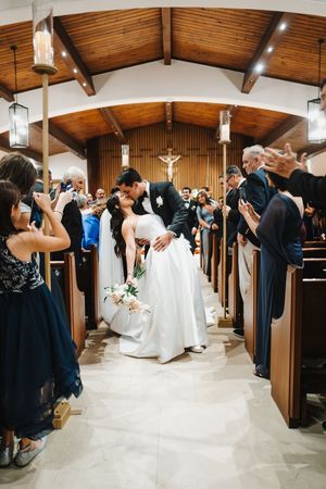 Wedding guests line the church aisle capturing photos of a couple exiting during their ceremony under wooden beams.