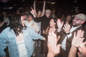 Crowd of people dancing and celebrating at a lively party or nightclub event with hands raised.