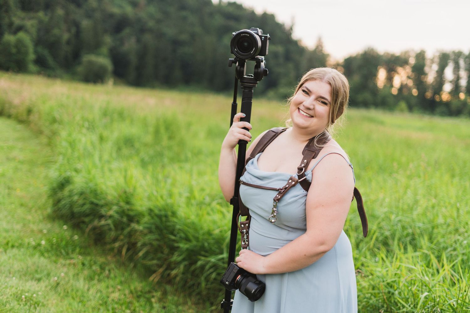 A person in a light blue dress poses in a sunny green field during a summer photo session.