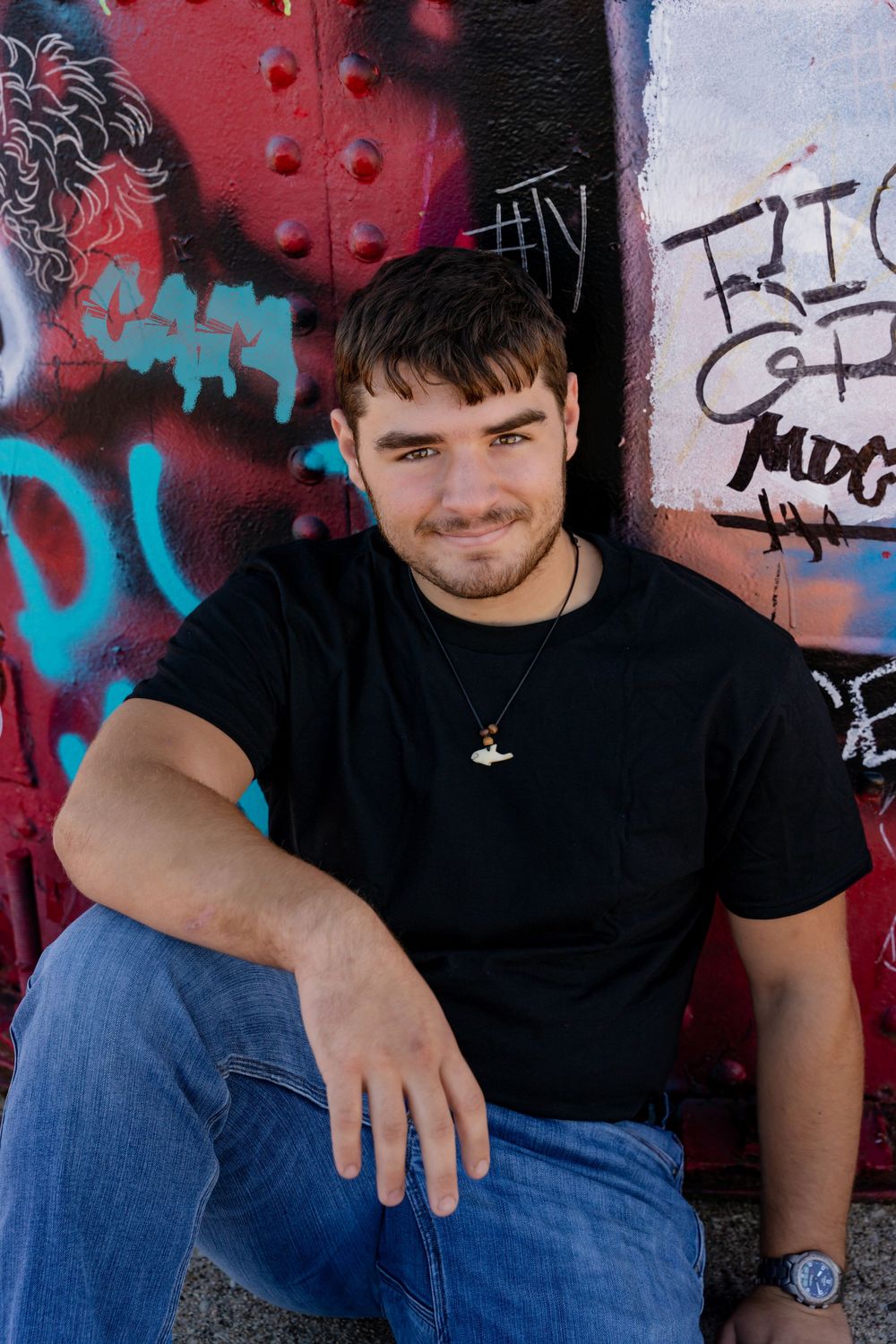 Person in black shirt and jeans posed against colorful graffiti wall in outdoor photo session.