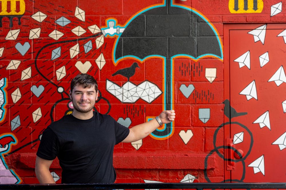 Paper airplanes and heart symbols decorate a vibrant red wall as someone poses against the artistic background.