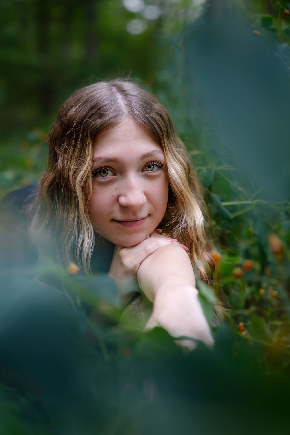 Artistic portrait through foliage with soft bokeh effect in natural lighting. Senior photography