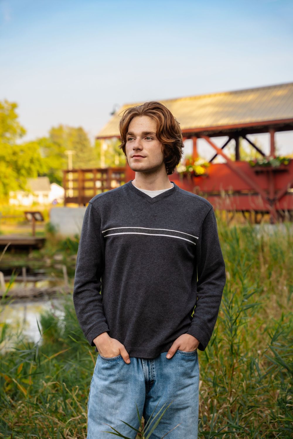Casual portrait by covered bridge wearing dark sweater in late afternoon light. Senior photography