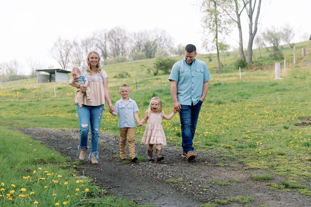 A family taking a stroll together on a dirt path through a springtime meadow filled with yellow wildflowers.