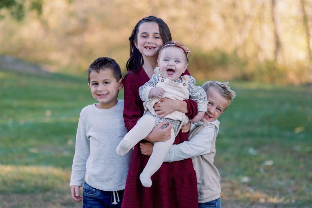 A family group poses together outdoors on a sunny autumn day in an open grassy field.