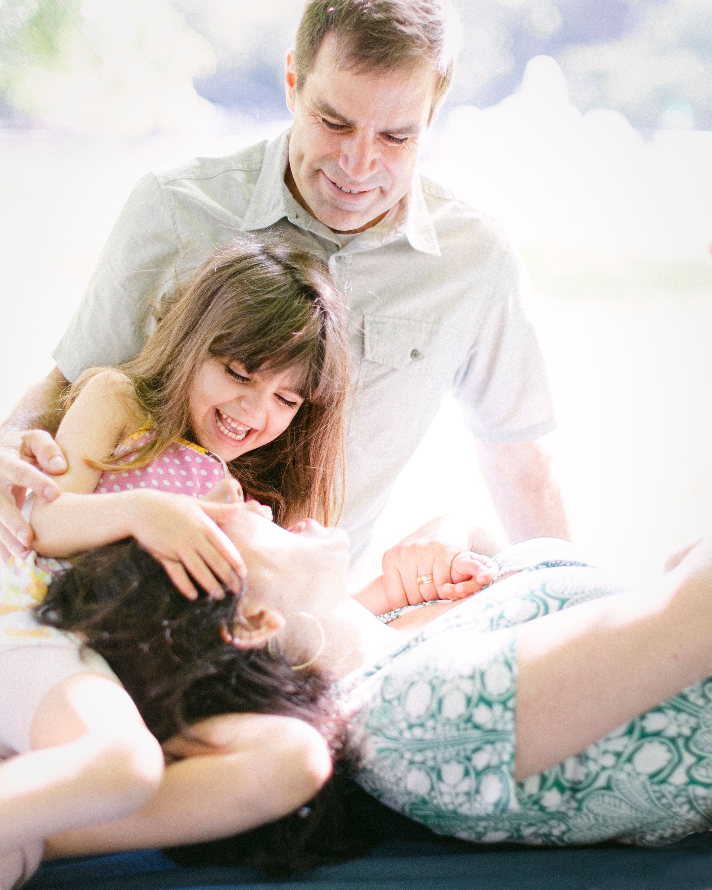 A playful family scene with everyone laughing and cuddling together in bright sunlight.