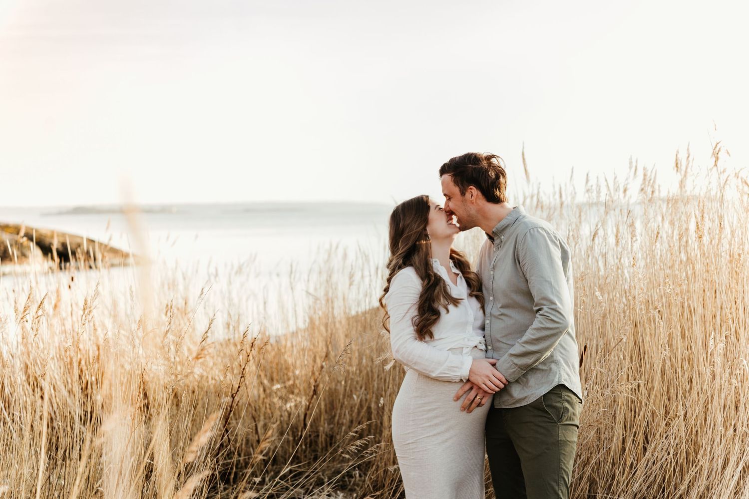 Romantic couple sharing an intimate moment among tall beach grass at sunset.