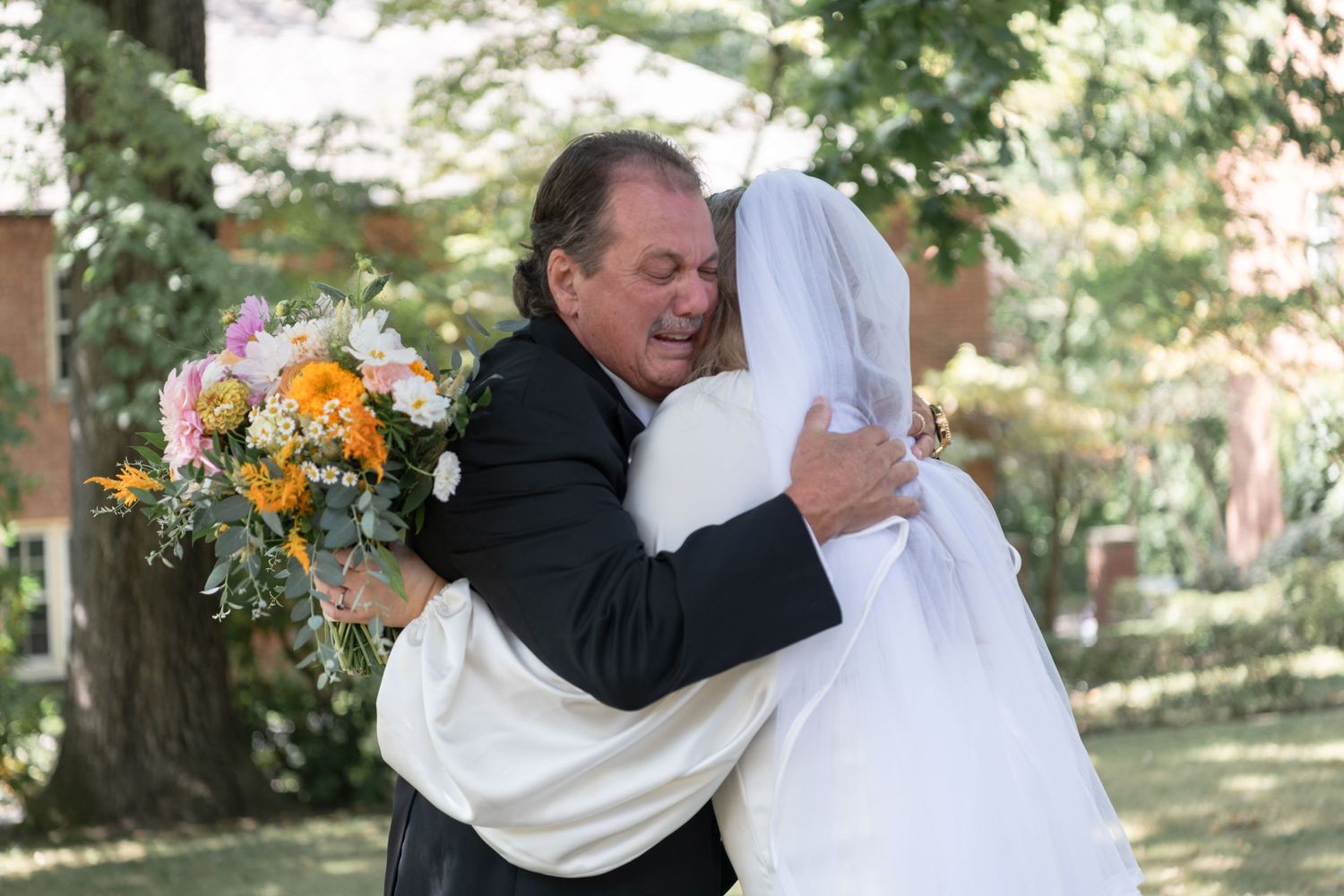 Emotional embrace during outdoor wedding celebration with colorful bouquet.