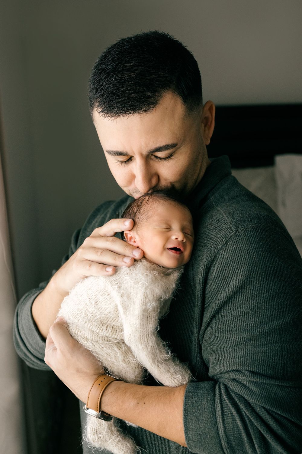 Father tenderly kissing his sleeping newborn baby wrapped in a soft white blanket.