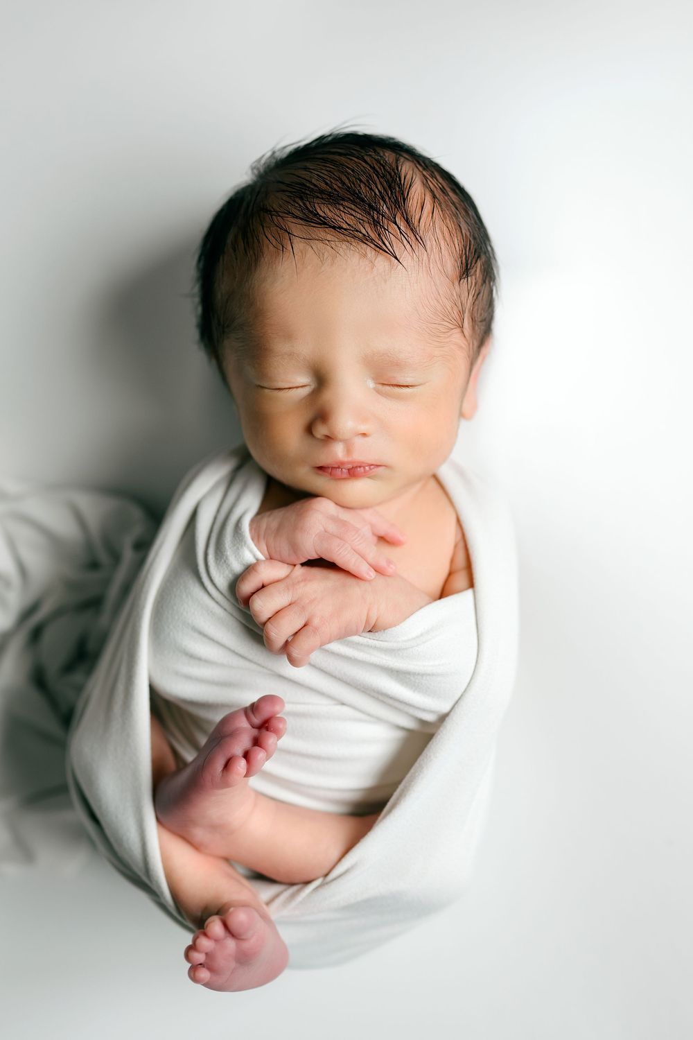 Peaceful sleeping newborn baby swaddled in a white wrap with tiny feet peeking out.
