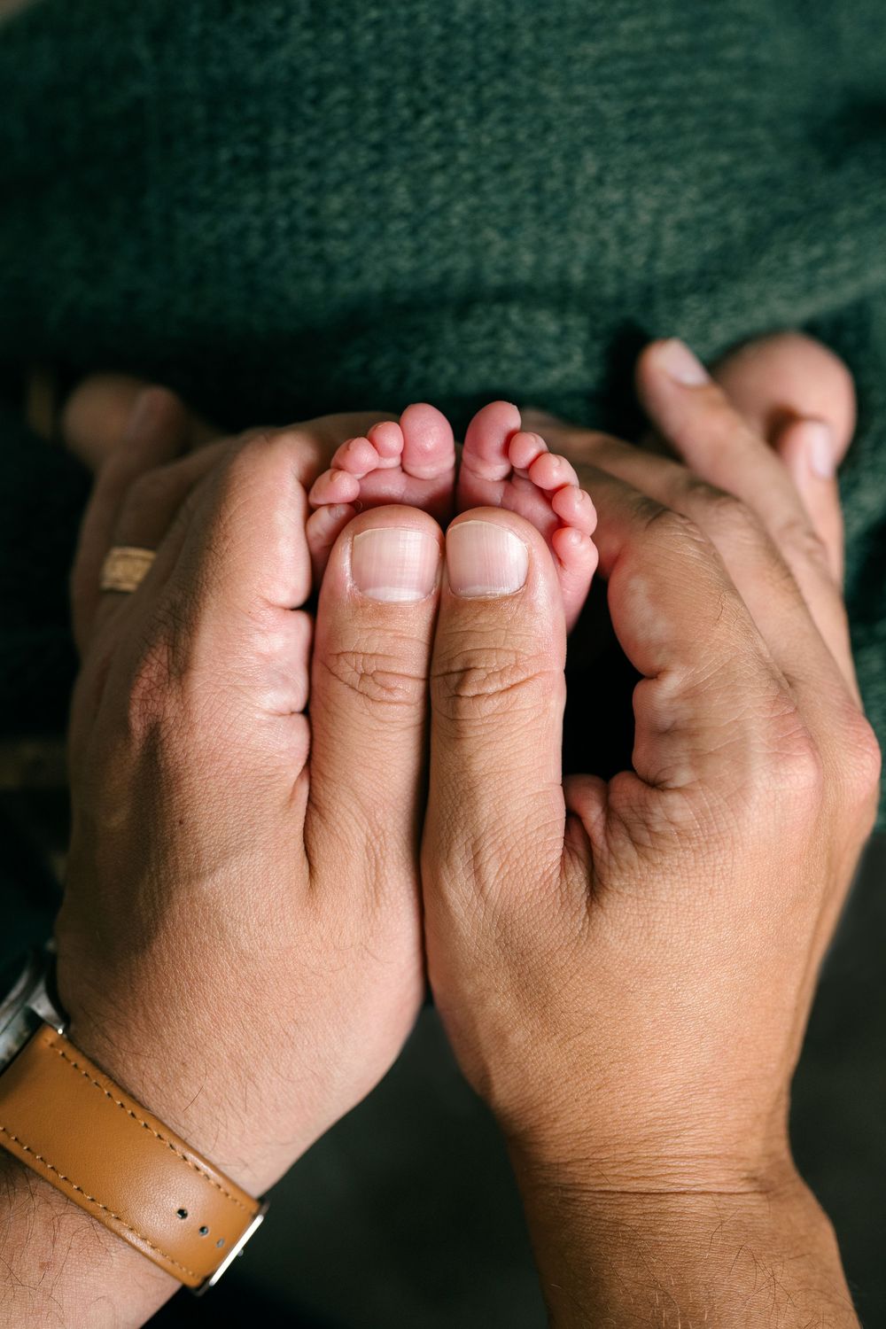 Close-up of parents hands gently holding their newborns tiny feet together.