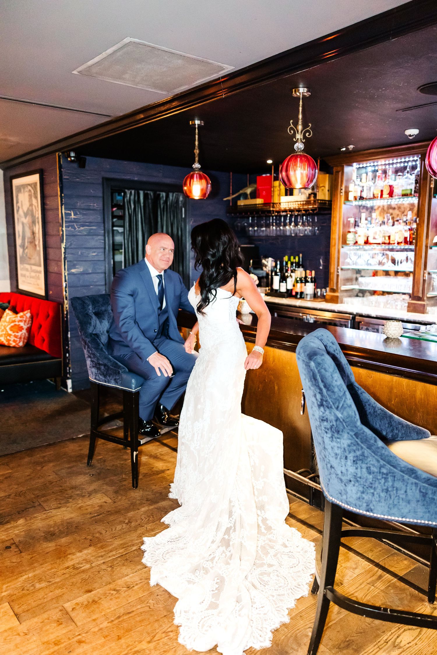 A couple dances together at a rustic bar venue with wooden floors and blue velvet seating during their wedding celebration.